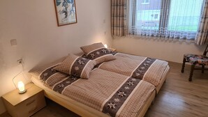 Quarto com uma cama, mesa de cabeceira com abajur, cadeira e janela com cortinas.
