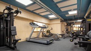 Et fitnessrum med træningsudstyr, løbebånd og vægtbænk.