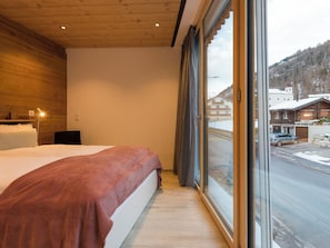Ein Schlafzimmer mit einem großen Bett, einer Holzbalkendecke und einem Fenster mit Blick auf eine verschneite Landschaft.