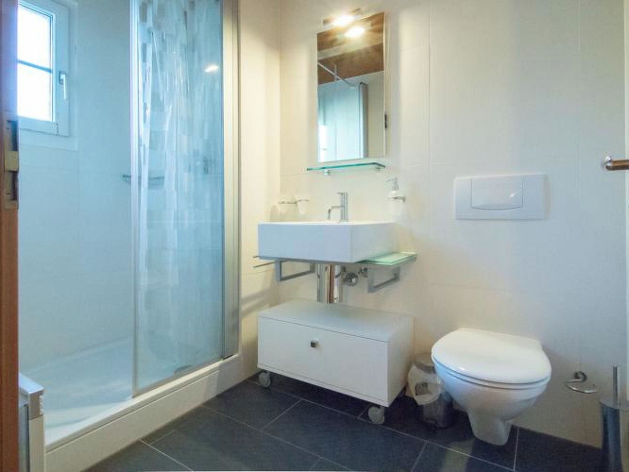 A bathroom with a glass shower enclosure, a white sink with a mirror above it, and a white toilet.