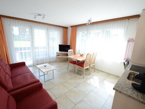 A modern living room with a red sofa, a dining table with chairs, a TV, and a kitchen area with a sink. - Mischi Appartement/Fewo 4-Bettwohnung Nr. 12 by Interhome (Saas-Fee)