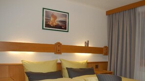 A hotel room with a bed, pillows, a nightstand, a wooden headboard, a framed picture on the wall, and a window with curtains. - Swiss Chalet Appartement/Fewo 2-Bettwohnung Nr. 5 by Interhome (Saas-Fee)