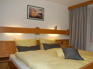 Ein Hotelzimmer mit einem Bett, Kissen, einem Nachttisch, einem Holzkopfende, einem gerahmten Bild an der Wand und einem Fenster mit Vorhängen.