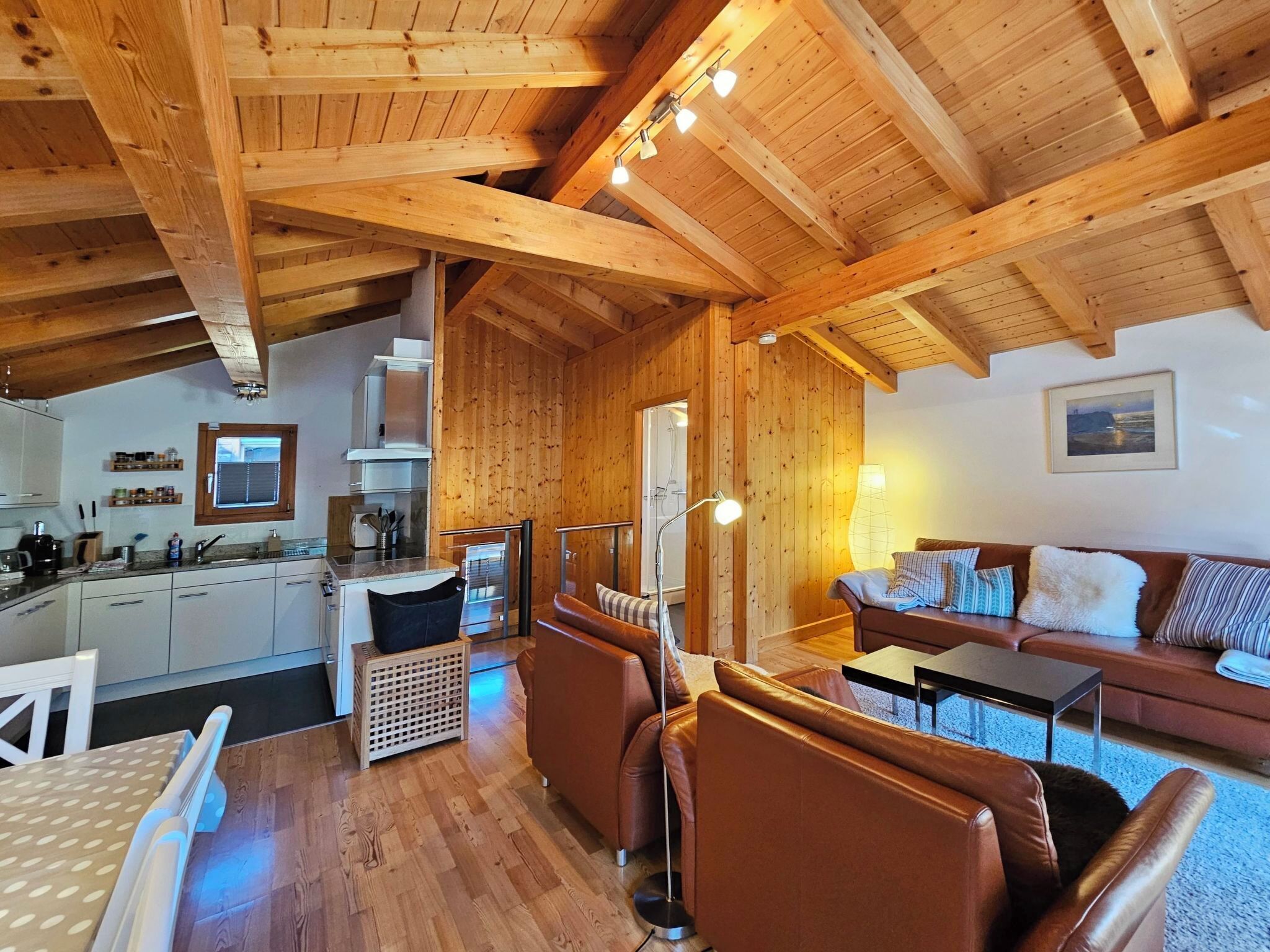 Un'ampia zona giorno con soffitto in legno, una cucina con mobili bianchi, un divano con cuscini decorati e un tavolo da pranzo con sedie.