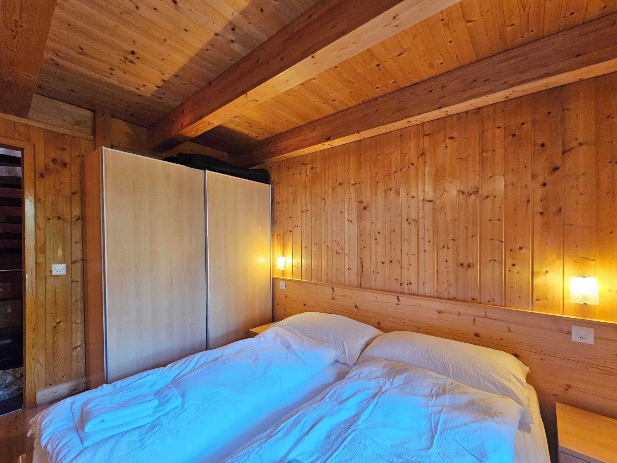 Une pièce aux murs lambrés, comprenant un lit, une armoire et des lampes fixées au mur.