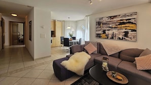 Een moderne woonkamer met een bank, een salontafel en een eethoek op de achtergrond.