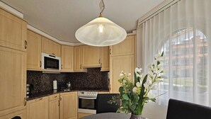 Een moderne keuken met houten kastjes, een magnetron, een fornuis en een eettafel met een schaal fruit en een vaas.