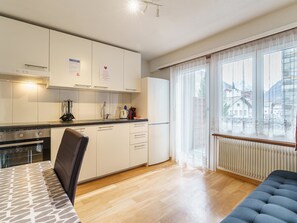 A modern kitchen with white cabinets, a stove, and a dining area with a table and chairs. - Haus City Appartement/Fewo Apt #4 by Interhome (Saas-Grund)