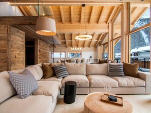 Ein modernes Interieur mit einer großen, winkelförmigen Couch, Holzbalken und großen Fenstern.