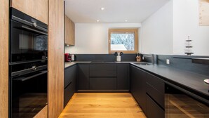 A modern kitchen with dark cabinetry, a wooden floor, and a window with a view of trees. - Berghof Penthouse Appartement/Fewo 8-Bettwohnung by Interhome (Saas-Fee)
