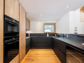 Eine moderne Küche mit dunklen Schränken, Holzboden und einem Fenster mit Blick auf Bäume.