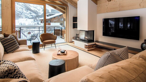 A cozy living room with a sofa, armchair, and coffee table, a fireplace, and a large window with a view of a snowy mountain. - Berghof Penthouse Appartement/Fewo 8-Bettwohnung by Interhome (Saas-Fee)