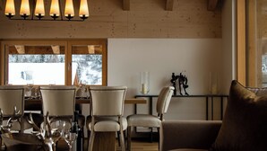 A dining area with wooden furniture, a table set with wine glasses, and a view of a snowy landscape through large windows. - Berghof Penthouse Appartement/Fewo 8-Bettwohnung by Interhome (Saas-Fee)