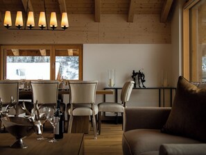 Ein Essbereich mit Holzmöbeln, einem Tisch, der mit Weingläsern gedeckt ist, und Blick auf eine verschneite Landschaft durch große Fenster.