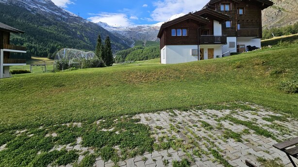Un chalet de dos pisos con un balcón, con montañas al fondo.