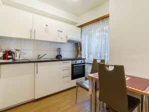 A compact kitchen with white cabinets, a stove, and a sink. There's a dining table with chairs. - Haus City Studio Apt #5 by Interhome (Saas-Grund)