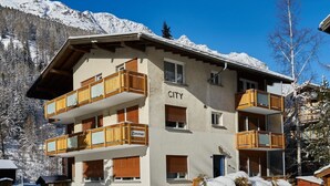 Ein mehrstöckiges Hotel mit Balkonen, eine verschneite Landschaft und Berge im Hintergrund.