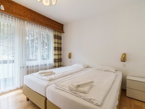 Ein Hotelzimmer mit einem Bett, zwei Nachttischen, einer Holzbalkendecke und einem Fenster mit leichtem Vorhang.