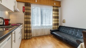A compact kitchen with a dining area, a sofa, and a window with patterned curtains. - Haus City Appartement/Fewo Apt #6 by Interhome (Saas-Grund)