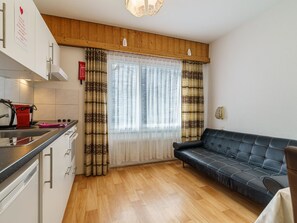 Eine kleine Küche mit Essbereich, einer Couch und einem Fenster mit gemusterten Vorhängen.