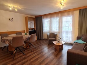 A furnished living room with a dining area, wooden flooring, and a view through the window. - Orion Appartement/Fewo 4-Bettwohnung Nr. 53 by Interhome (Saas-Grund)