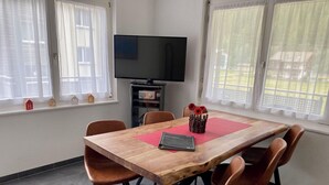 Een eetruimte met een houten tafel, zes stoelen, een flatscreen televisie en een raam met gordijnen.