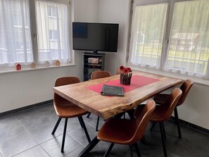 Ein Essbereich mit einem Holztisch, sechs Stühlen, einem Flachbildfernseher und einem Fenster mit Vorhängen.