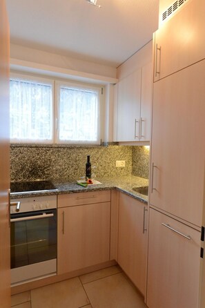 Eine kleine Küche mit Granitarbeitsplatten, einem eingebauten Backofen und einem Fenster mit Vorhängen.