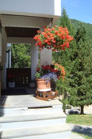 Ein Haus mit Veranda, einem Topf mit roten Blumen und einem kleinen Holzschemel.
