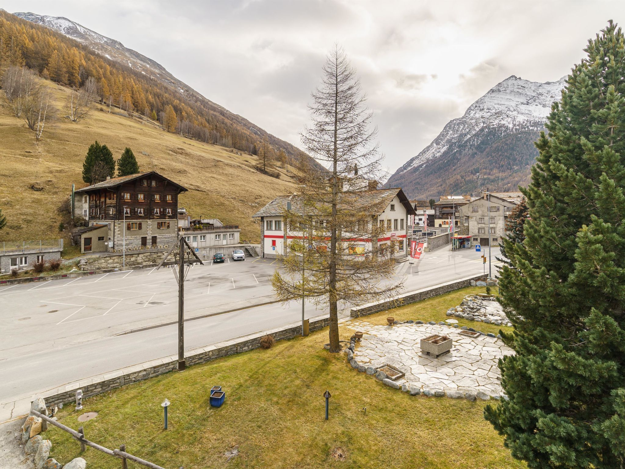 Un village de montagne aux bâtiments traditionnels, doté d’un parking et offrant une vue sur des montagnes enneigées.