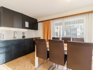 A modern kitchen with black cabinets, a stainless steel sink, and a dining area with brown chairs and a wooden table. - Haus City Appartement/Fewo Apt #3 by Interhome (Saas-Grund)