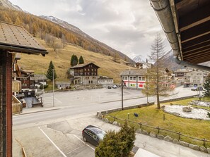 A parking lot with a mountain backdrop, a building with a wooden facade, and a clear sky. - Haus City Appartement/Fewo Apt #3 by Interhome (Saas-Grund)