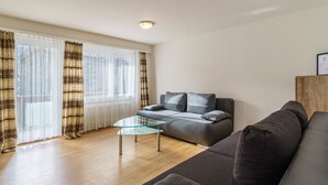 Ein modernes Wohnzimmer mit einer Couch, einem Glastisch und einem großen Fenster mit Vorhängen.