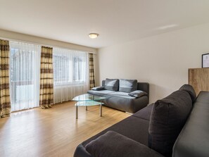 Ein modernes Wohnzimmer mit einer Couch, einem Glastisch und einem großen Fenster mit Vorhängen.