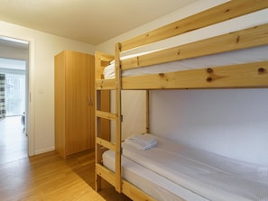 Ein Etagenbett mit Holzleiter, ein Kleiderschrank und ein Fenster mit Vorhängen.