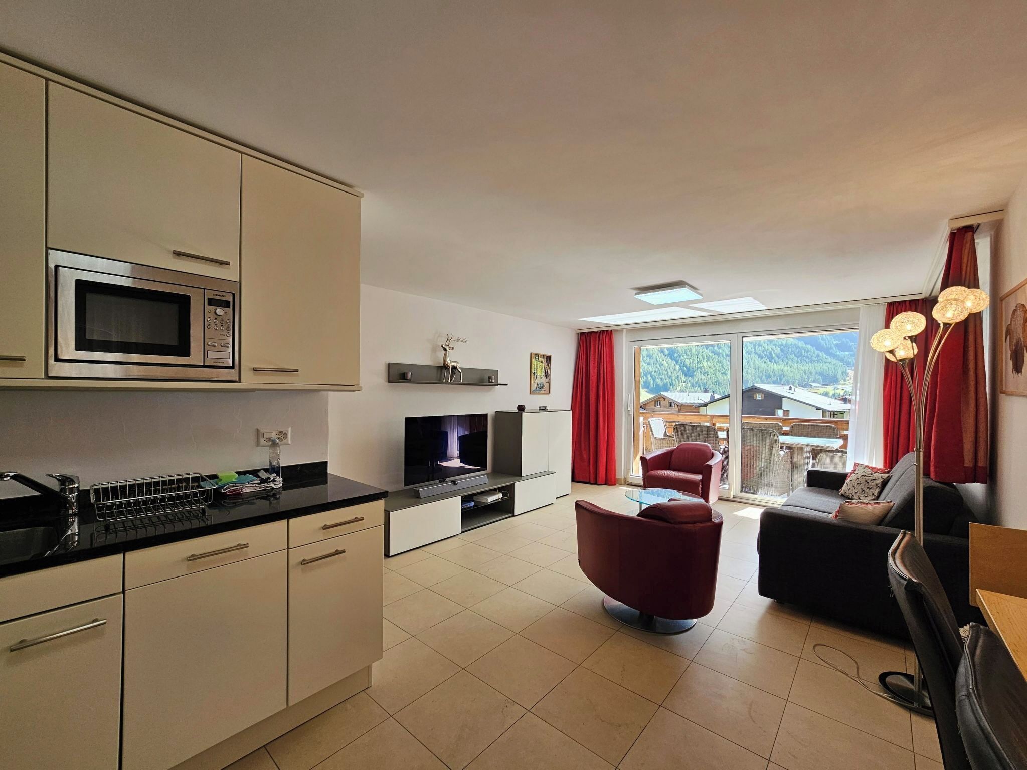 A modern kitchen with a microwave, a dining area with a table and chairs, and a living room with a sofa and a TV.