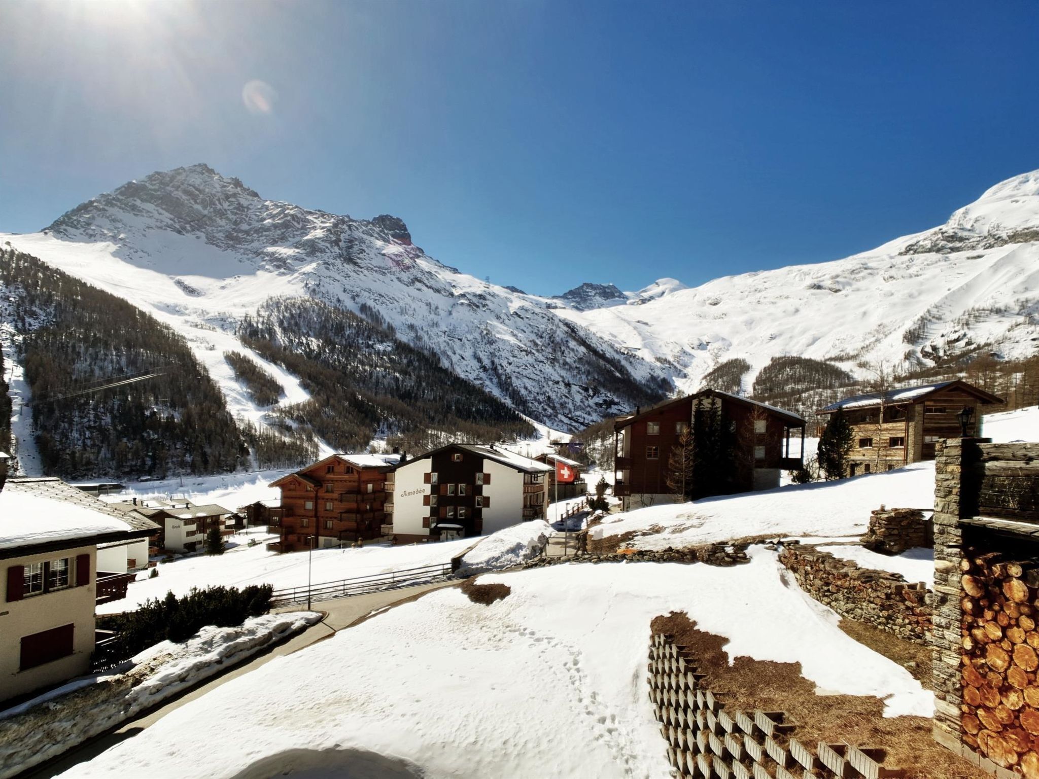 Un chalet de montagne avec des cabanes en rondins, un télésiège et, en arrière-plan, des montagnes enneigées.