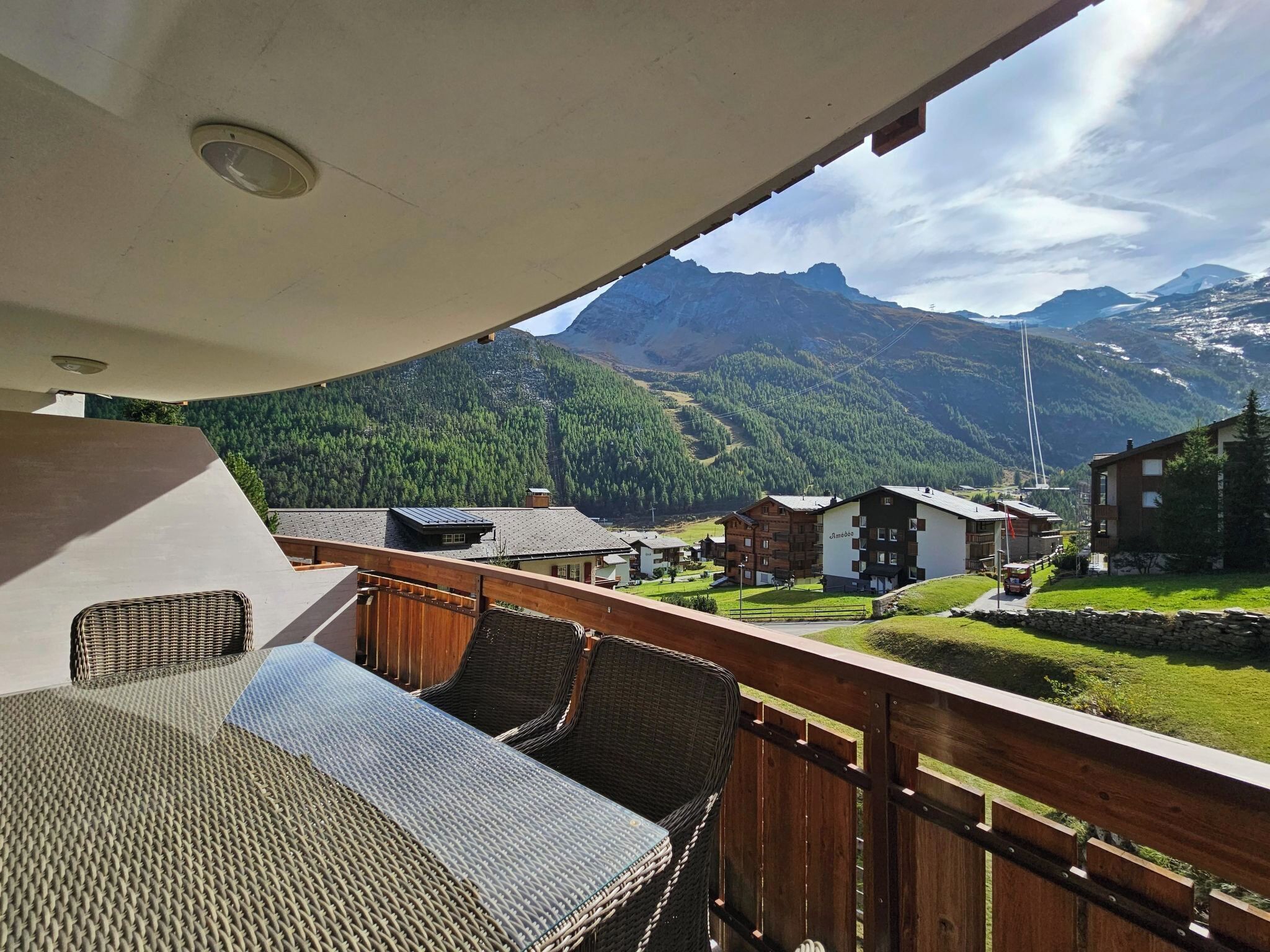 Ein Balkon mit Korbmöbeln mit Blick auf eine gebirgige Landschaft und Gebäude.