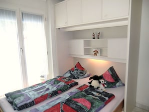 Un dormitorio con cama, almohadas, una mesita de noche y una estantería con objetos decorativos.