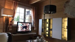 Una habitación acogedora con televisor, una mesita de centro de vidrio y un mueble moderno con estantes iluminados.
