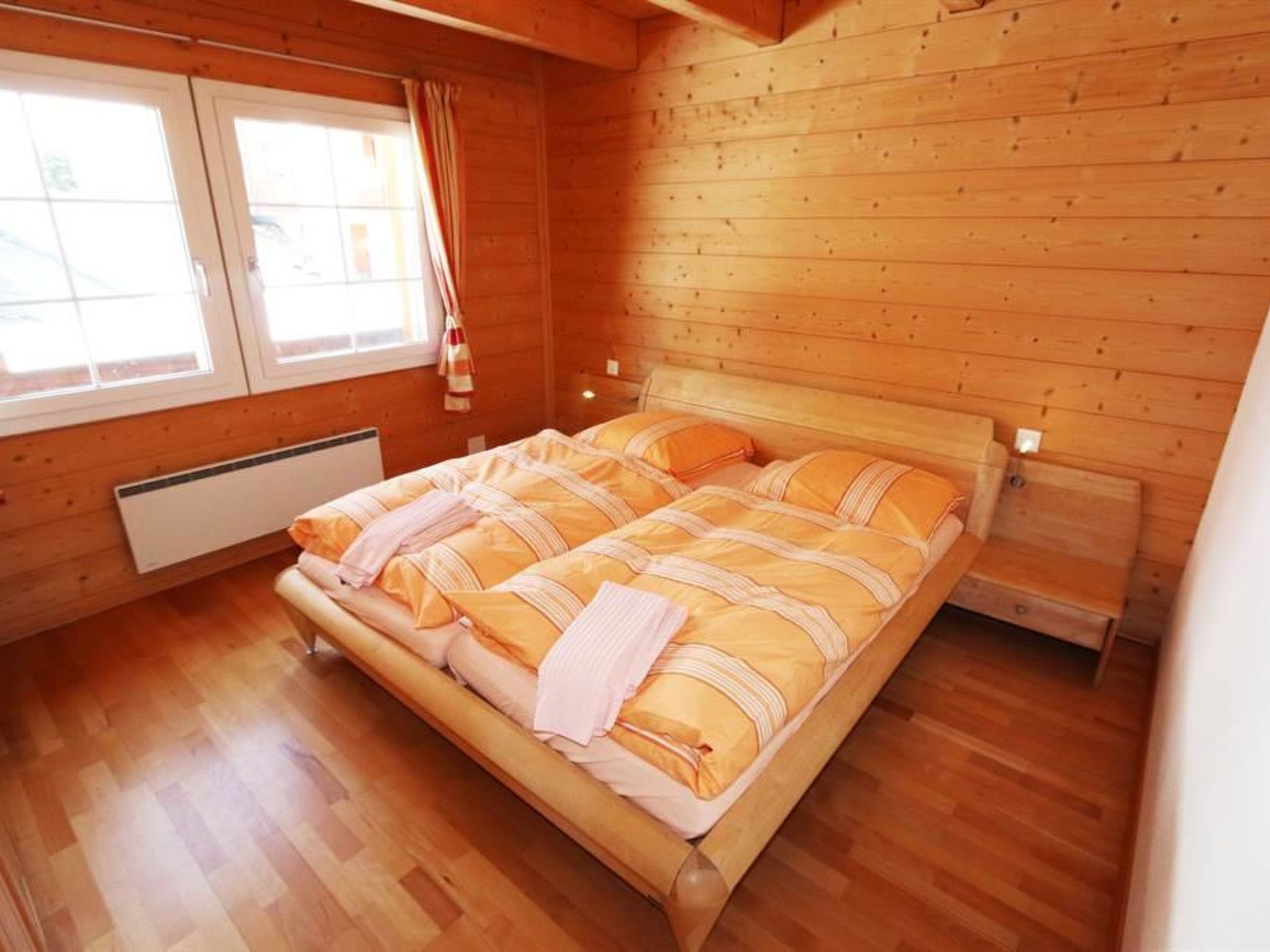 Ein Zimmer mit Holzwänden, einem Bett, einem Heizkörper und einem Vorhangfenster.