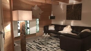 Una sala de estar moderna con un sofá de cuero oscuro, techo de madera, lámpara colgante y una alfombra estampada.