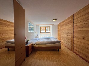 A bedroom with a wooden floor, a bed, a nightstand, a dresser, a window, and a ceiling light. - Ferienhaus Lomatte 1758 Appartement/Fewo Appartement/Fewo by Interhome (Saas-Fee)
