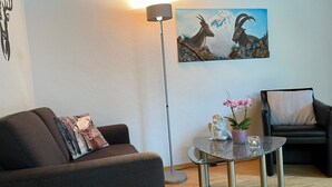 Un salon comprenant un canapé, une table basse ronde, un lampadaire, un tableau représentant des chèvres de montagne et un fauteuil.
