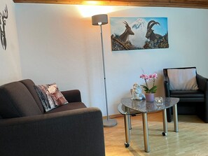 Ein Wohnzimmer mit einer Couch, einem runden Couchtisch, einer Stehlampe, einem Gemälde von Bergezigen und einem Sessel.