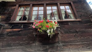 Un immeuble en bois à plusieurs étages, doté d’un balcon, d’une jardinière remplie de fleurs et d’une enseigne indiquant l’année 1758.