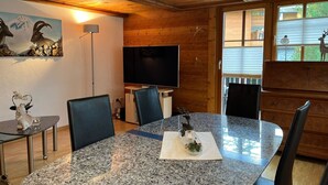 Un coin repas comprenant une table en granit, des chaises, un téléviseur et un mur en bois orné d’un tableau.