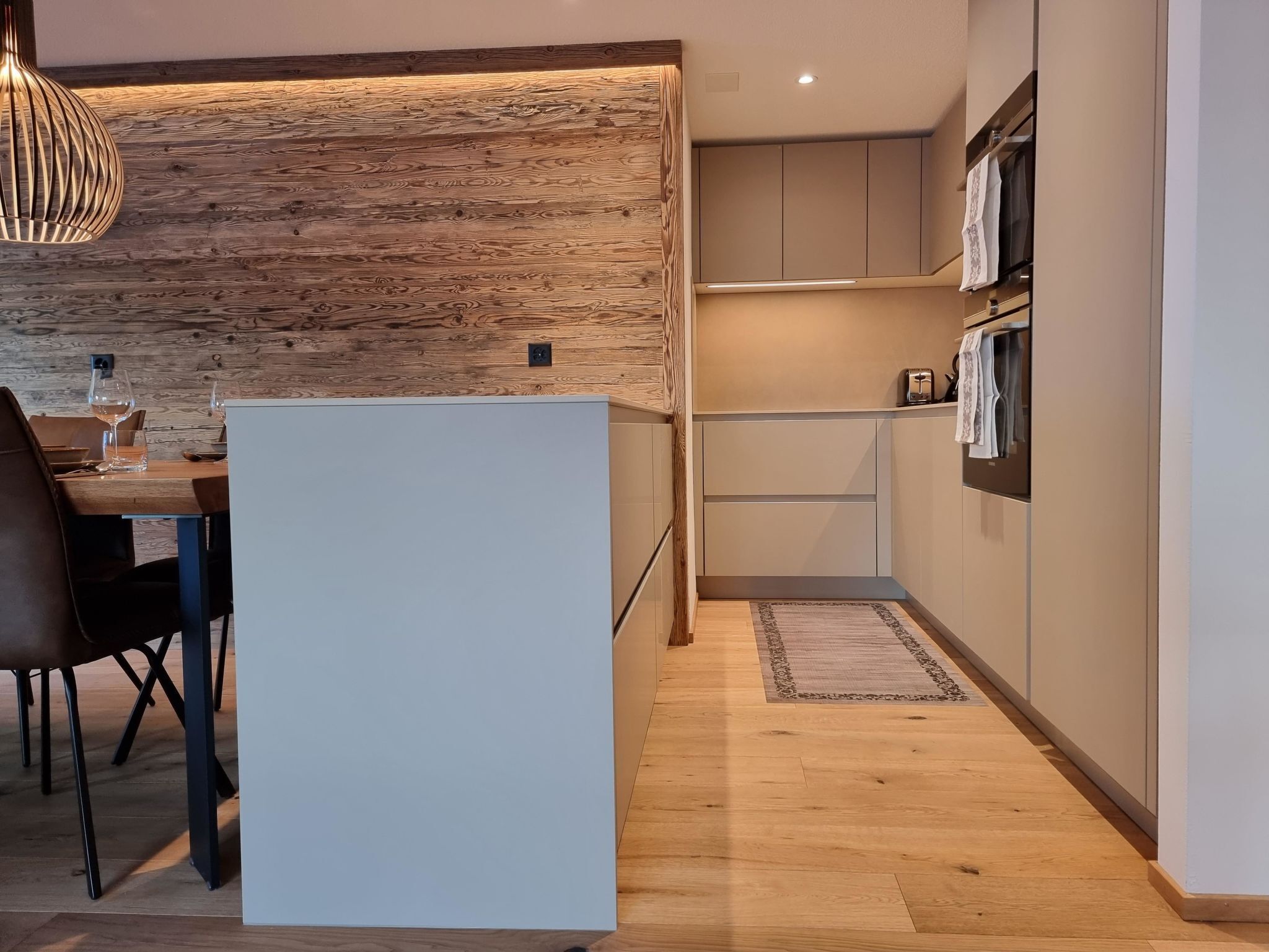 Une cuisine moderne agrémentée d’éléments en bois, un coin repas avec une table et des chaises, et des placards intégrés.