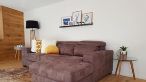 Een moderne woonkamer met een bruine modulaire bank, een glazen salontafel, een klein bijzettafeltje en een wandplank met ingekaderde foto’s.