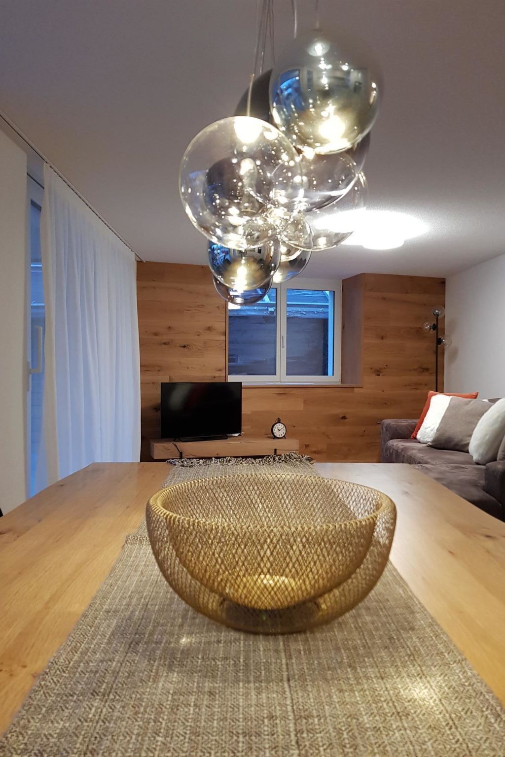 Una habitació amb una taula de dinar de fusta, una cistella de vimet, un televisor de pantalla plana i una finestra amb parets de fusta.